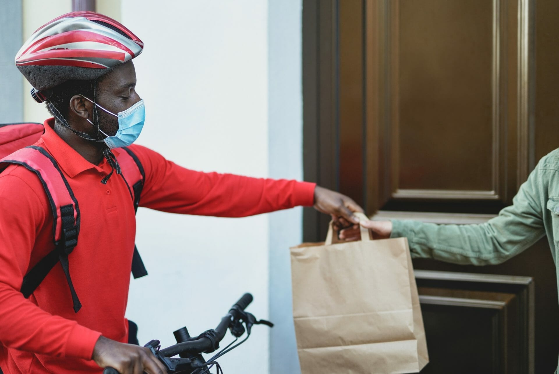 African food delivery man with bicycle and paper bag wearing surgical face mask