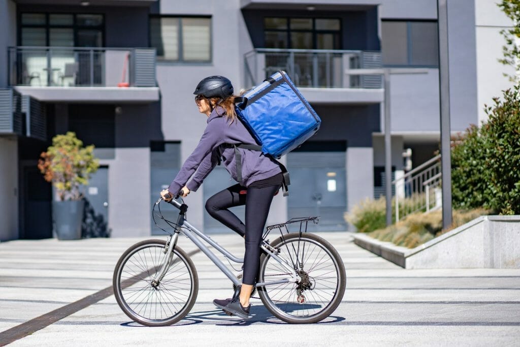 The delivery person is on an electric bike with a food delivery bag on her back.